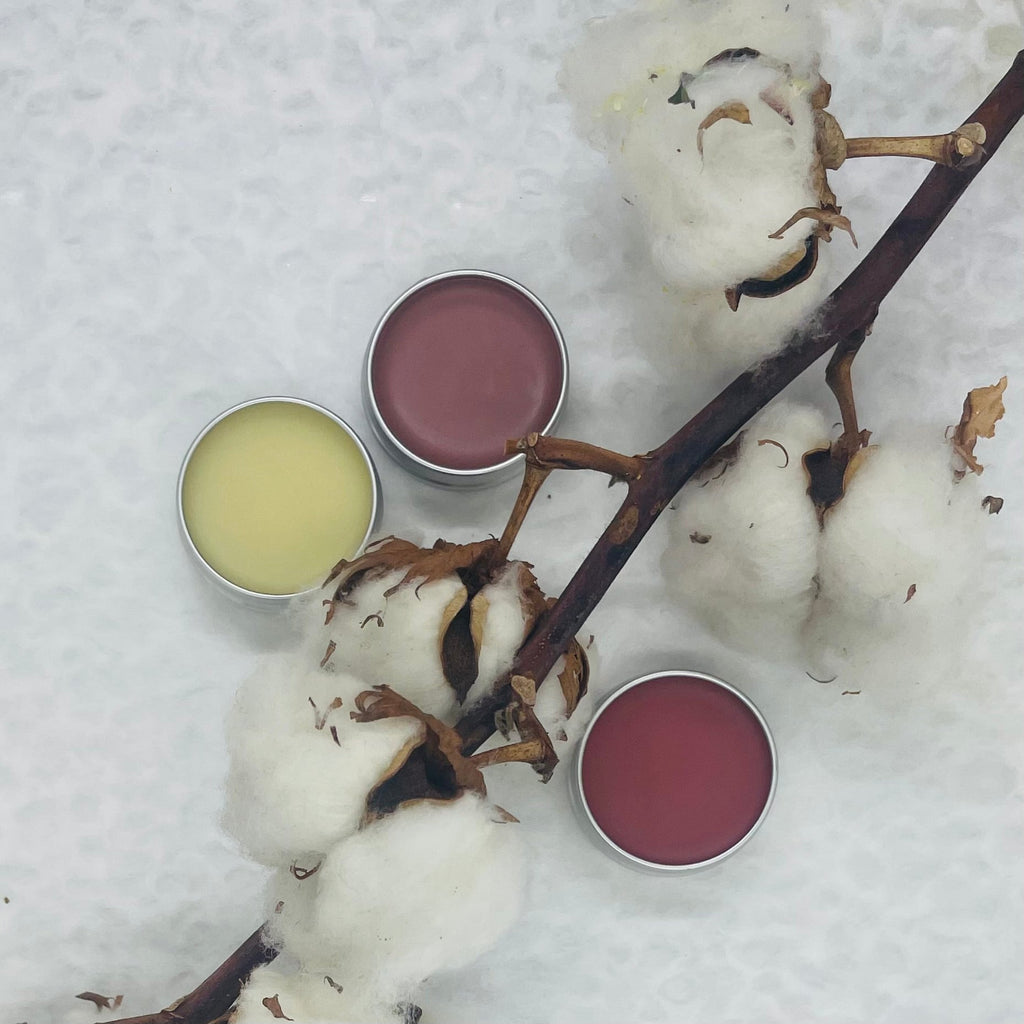 3 different colour lip balms with cotton twig on white textured background